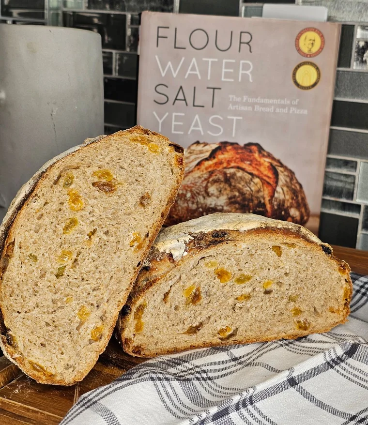Розріз хліба з родзинками поруч із книгою Flour Water Salt Yeast